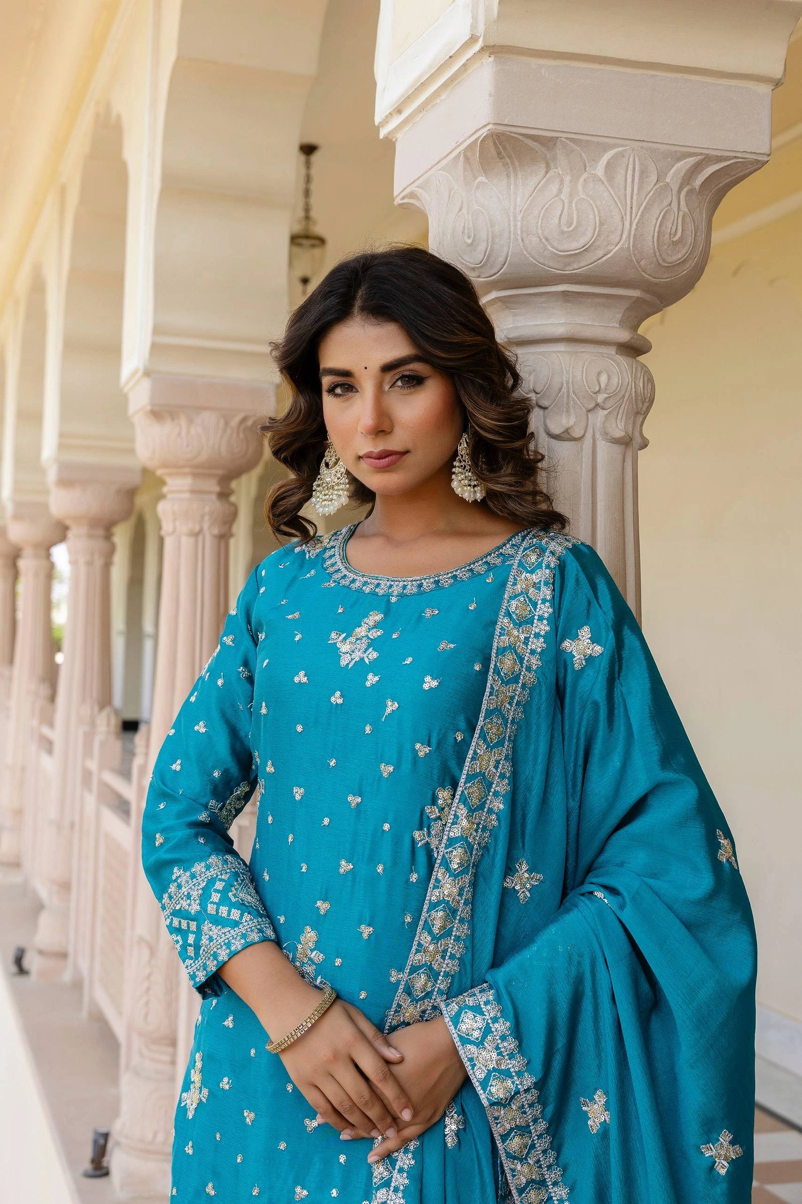 Woman in a blue traditional outfit with white patterns standing in an architectural setting.