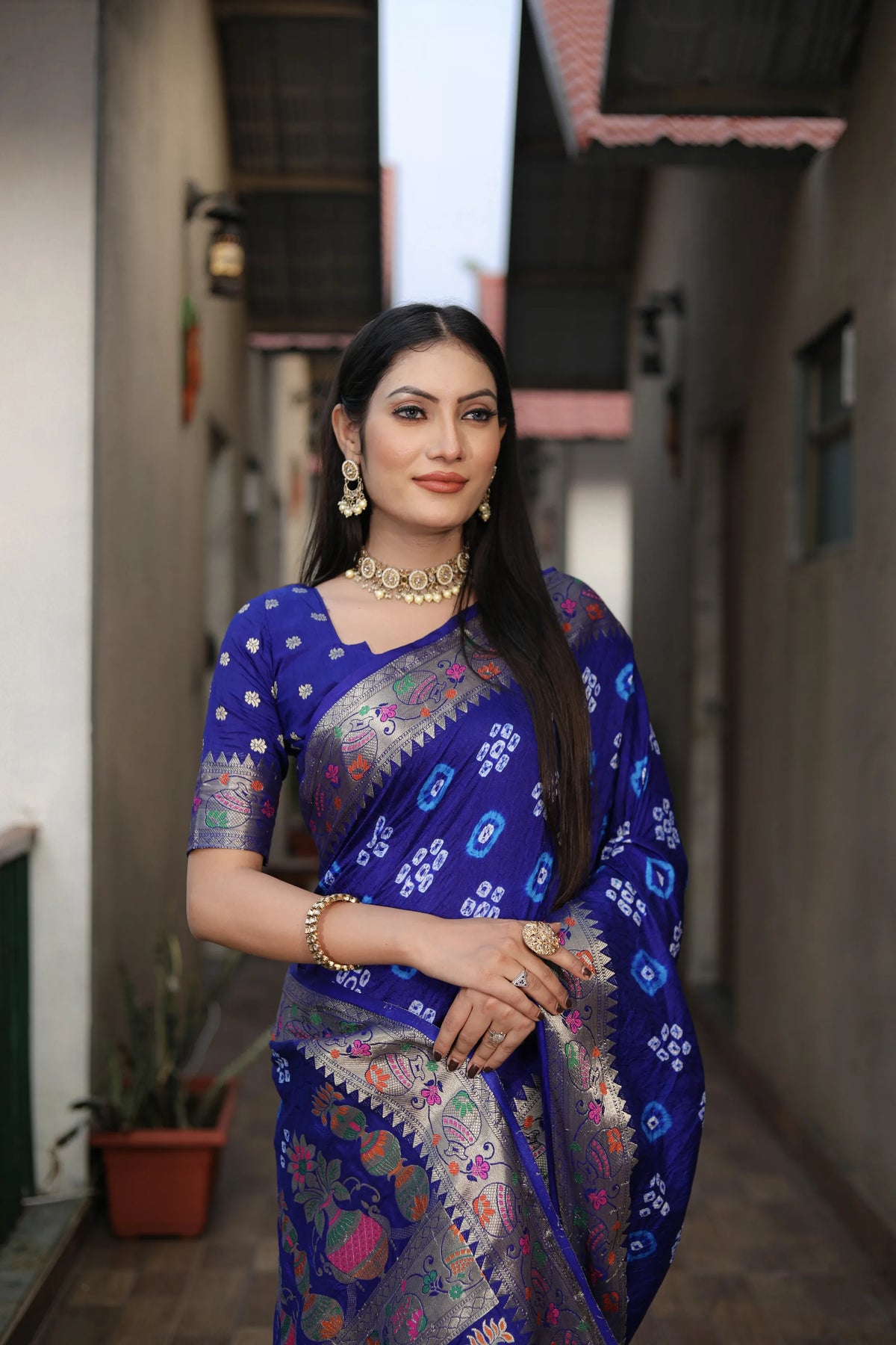 Woman in a blue saree with a patterned border standing in an outdoor setting.