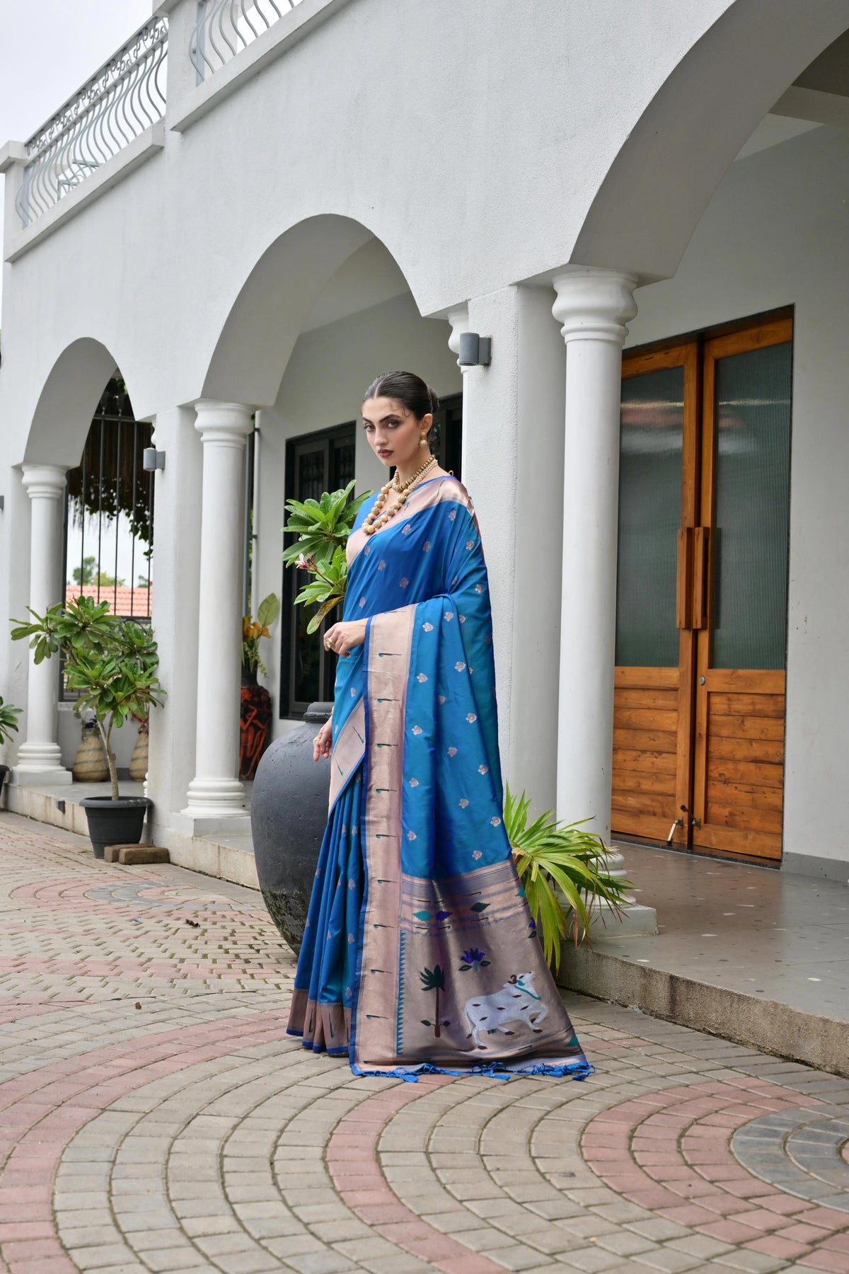 Woman in a blue saree standing in front of a white building with columns.