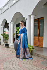 Woman in a blue saree standing in front of a white building with columns.