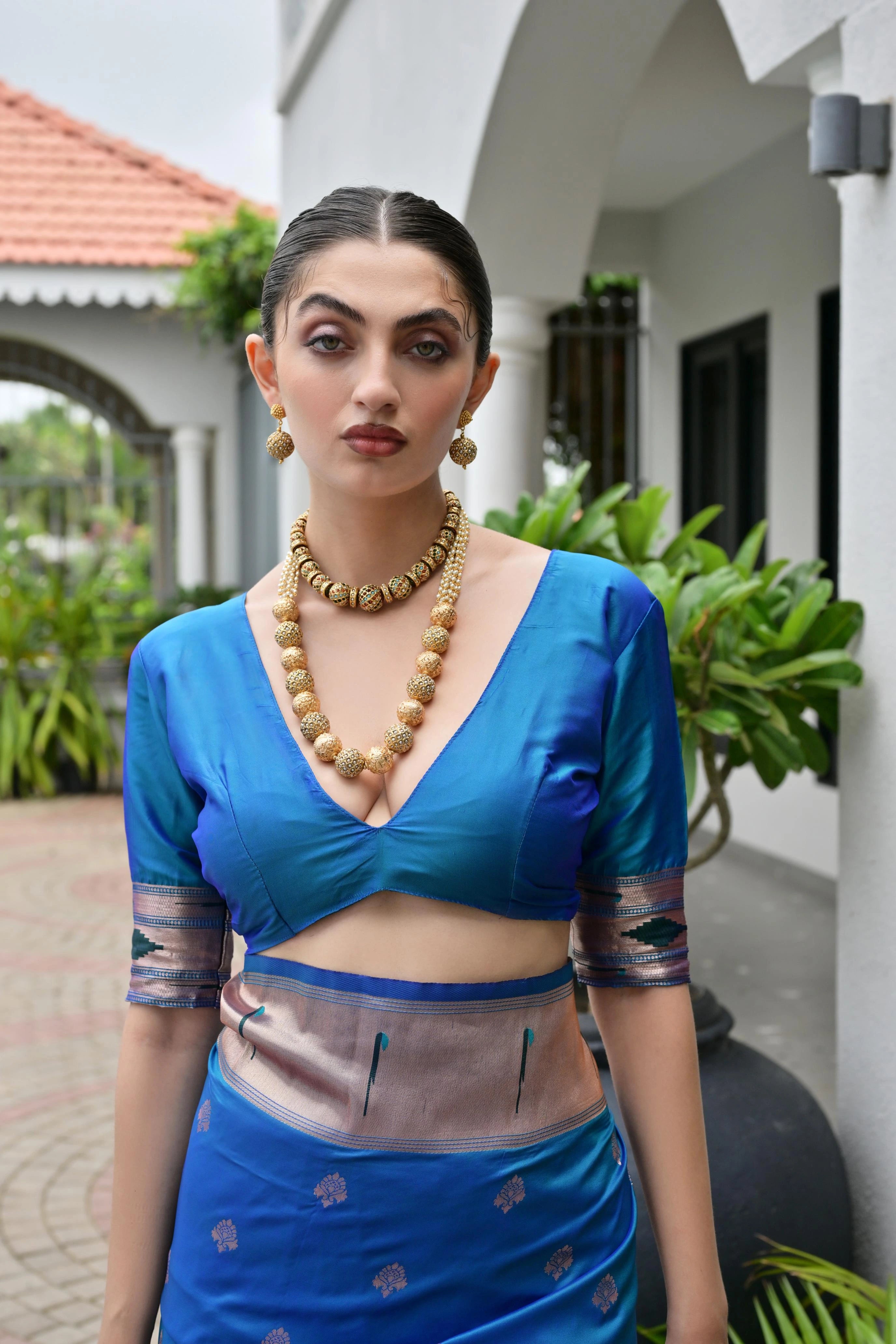 Woman wearing a blue traditional outfit with a necklace, standing outdoors.