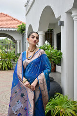 Woman in a blue saree standing outdoors with plants and a building in the background