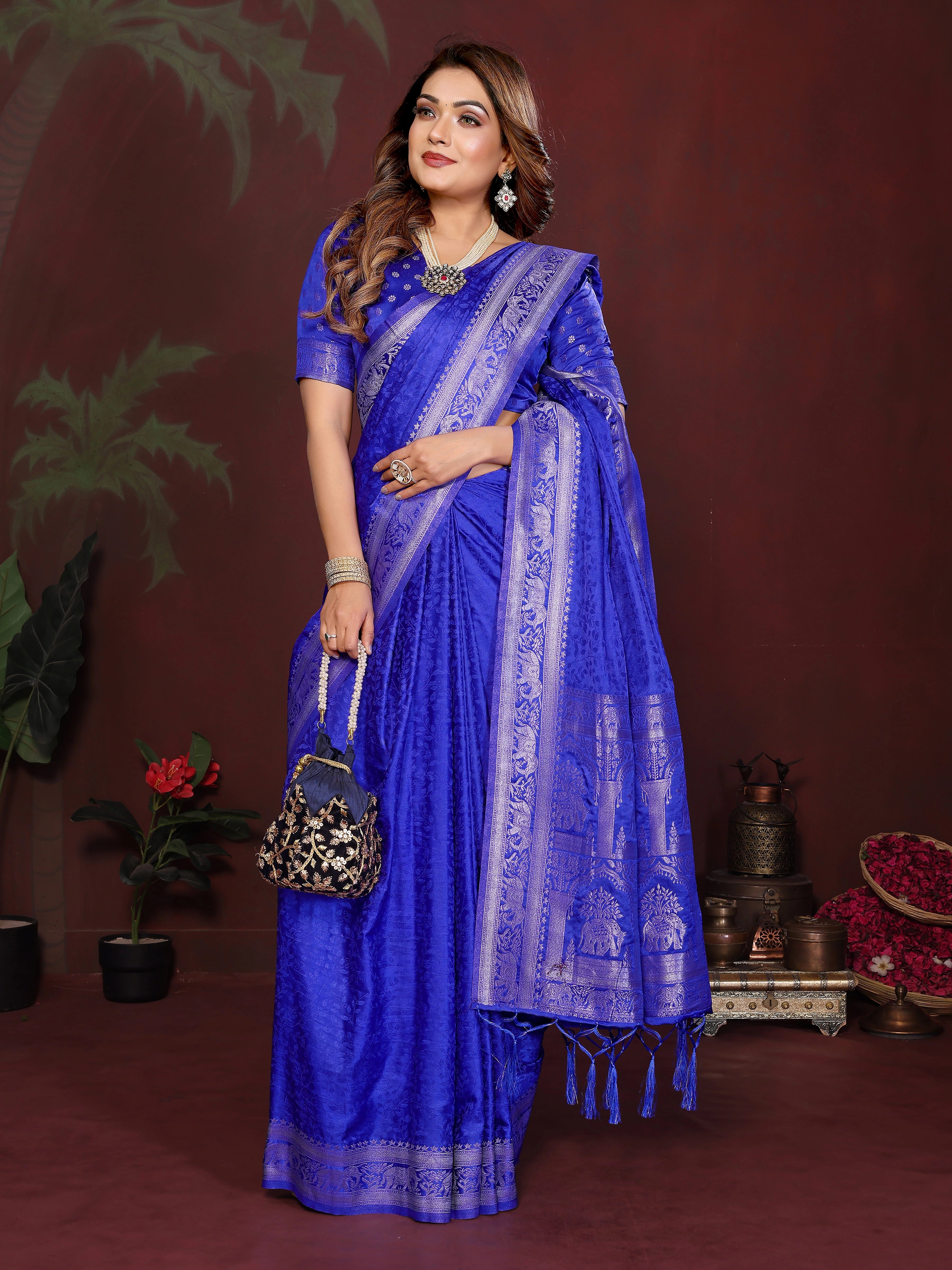 Woman wearing a blue saree with a matching blouse, standing against a dark background.