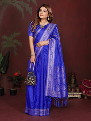Woman wearing a blue saree with a matching blouse, standing against a dark background.