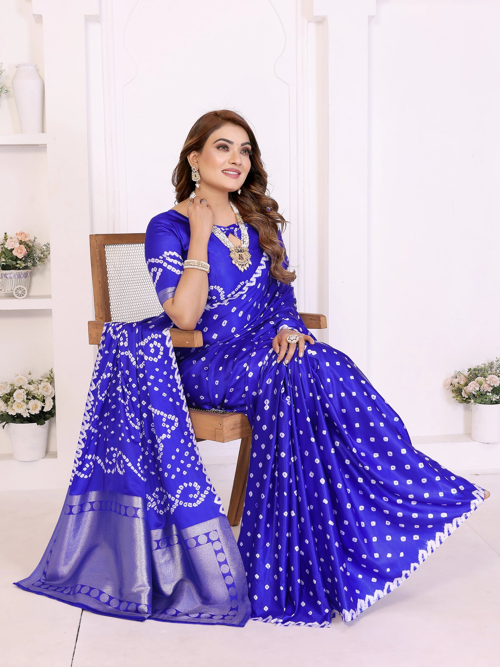 Woman wearing a blue saree with white patterns sitting on a chair.