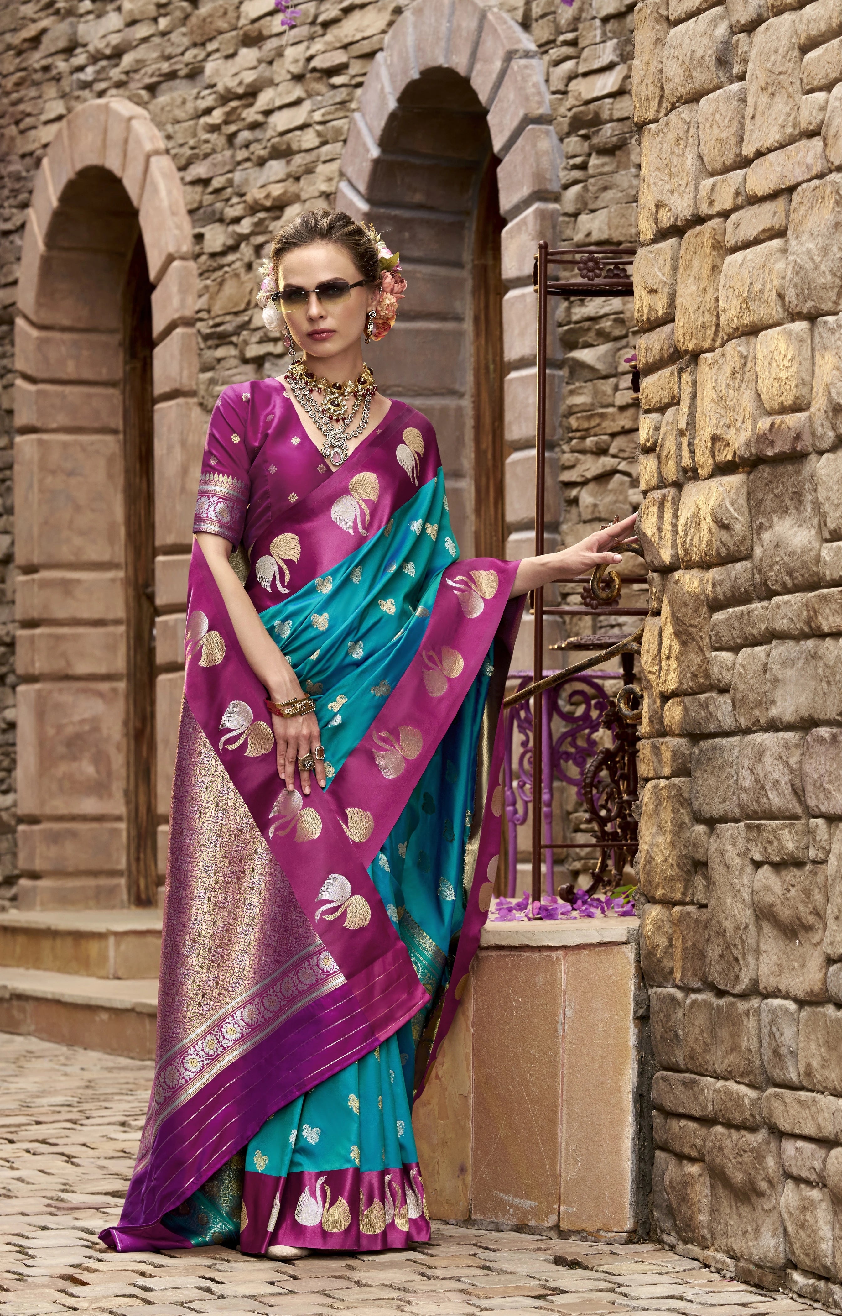 Woman in a traditional saree standing in front of stone arches.