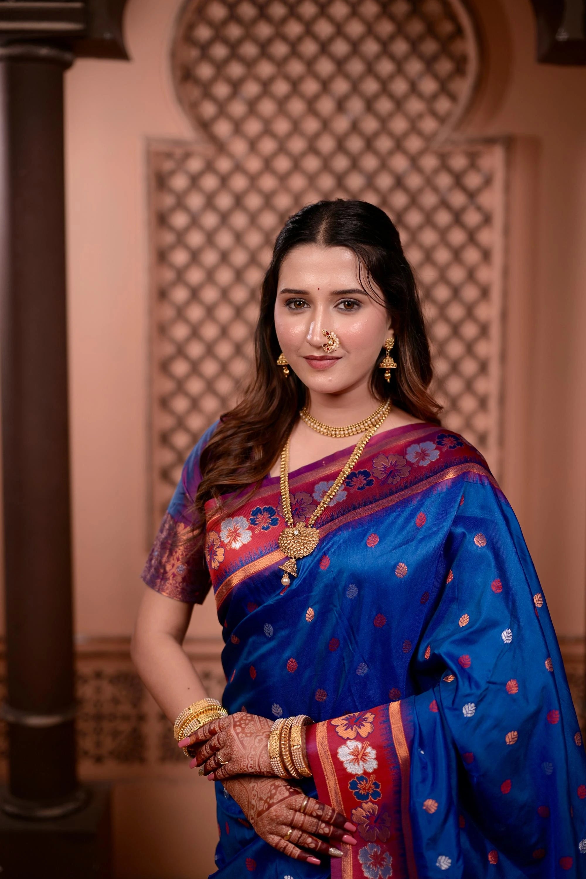 Woman in a blue saree with floral patterns against an ornate wall.