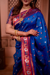 Woman wearing a blue saree with floral patterns and gold jewelry indoors.