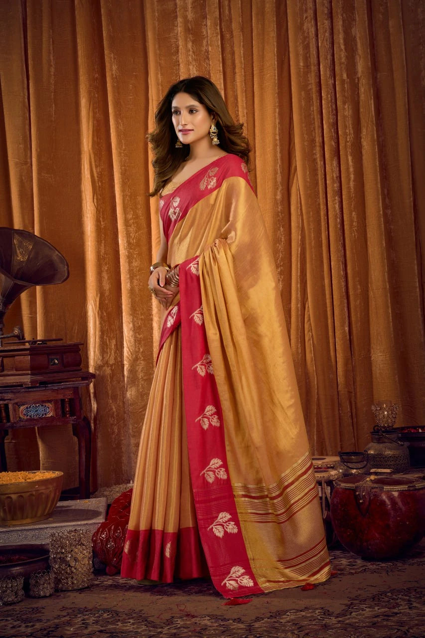 Woman in a traditional yellow and red saree standing in front of a decorative background.
