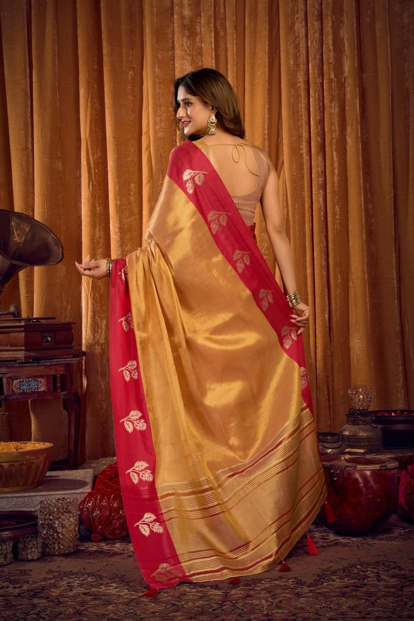 Woman in a yellow and red saree standing in a room with wooden furniture and curtains.
