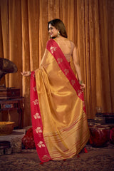 Woman in a yellow and red saree standing in a room with wooden furniture and curtains.