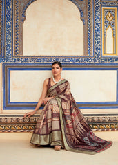 Woman in a traditional saree sitting against an ornate wall.