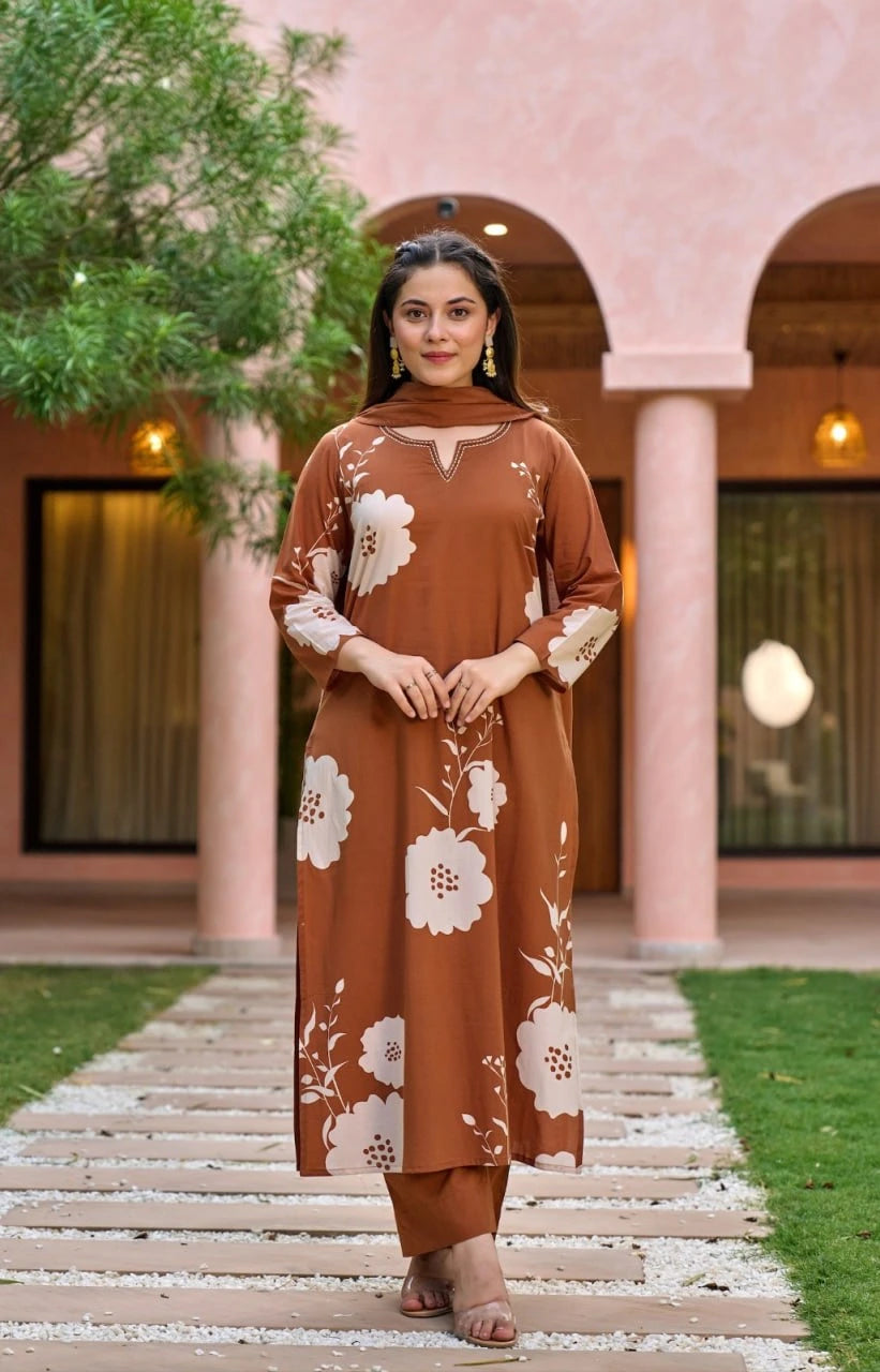 A full-length shot of the woman standing on a stone pathway in a courtyard. She is wearing a straight-cut terracotta kurta with matching trousers, showcasing the bold white flower and stem patterns distributed across the garment.