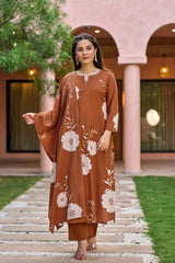 Woman wearing a brown floral outfit standing on a pathway with greenery and a building in the background.