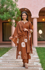 Woman in a brown floral outfit standing on a stone path with a pink building in the background