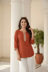 Woman wearing a rust-colored top with white pants in an elegant indoor setting.