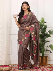 Woman wearing a brown saree with floral patterns in a room with a plant and decorative items.