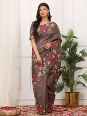 Woman wearing a brown saree with floral patterns standing indoors next to a plant.