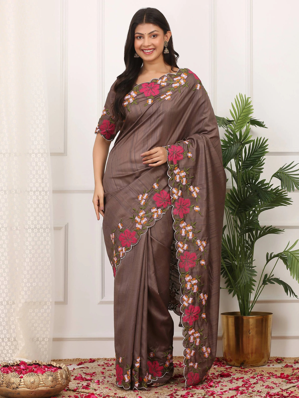 Woman wearing a brown saree with floral patterns standing indoors.