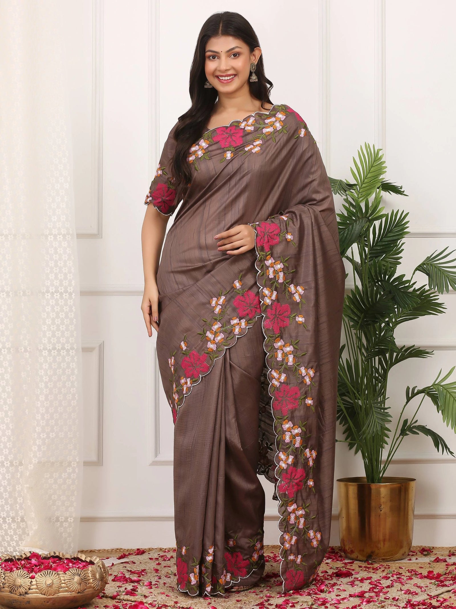 Woman wearing a brown saree with floral patterns standing indoors.