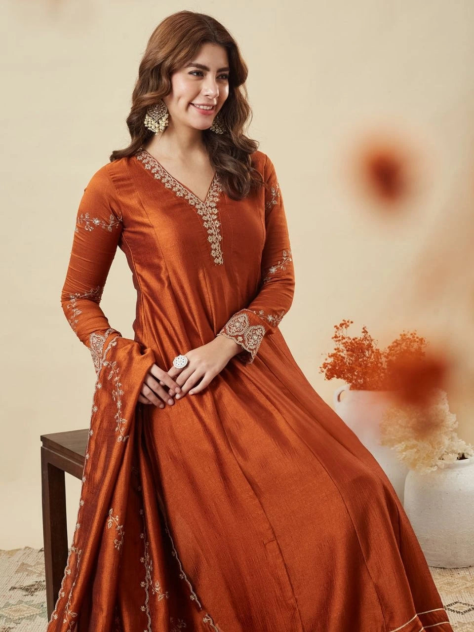 Woman wearing an orange dress with intricate patterns, sitting on a chair.