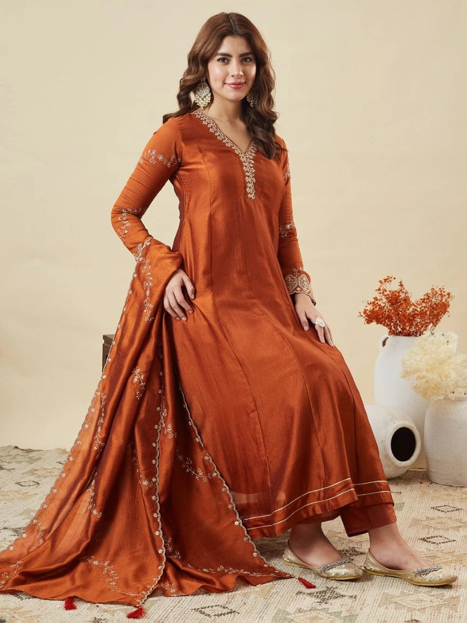 Woman wearing a rust-colored traditional outfit with intricate designs on a beige background
