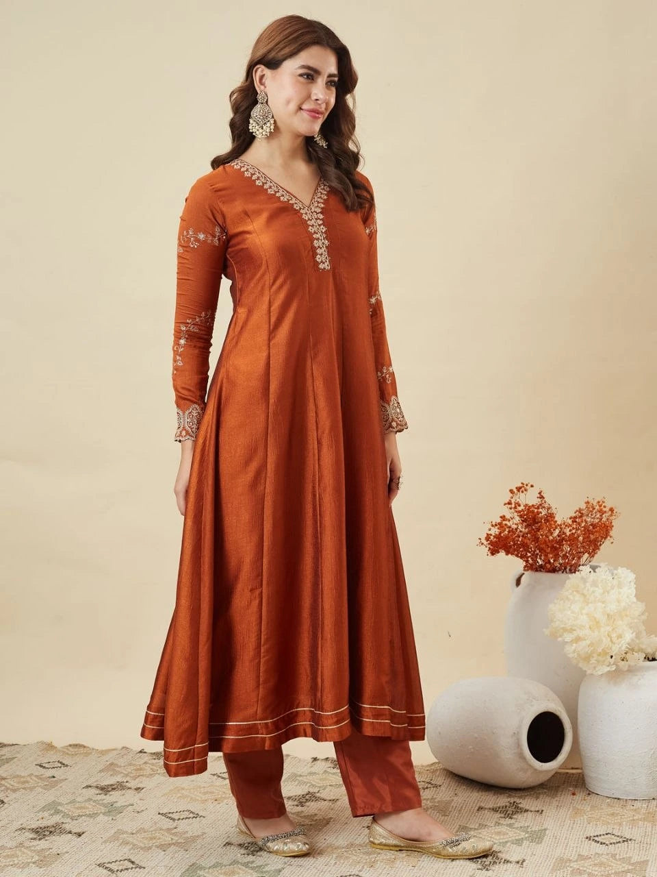 Woman wearing a rust-colored traditional outfit with intricate designs on a beige background