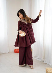 Woman in a burgundy outfit with white patterns standing in a room with white curtains.