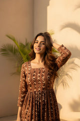 Woman in a brown patterned dress standing against a neutral background with plants.