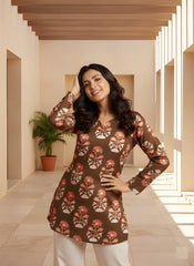 Woman wearing a brown floral patterned dress in a sunlit hallway.