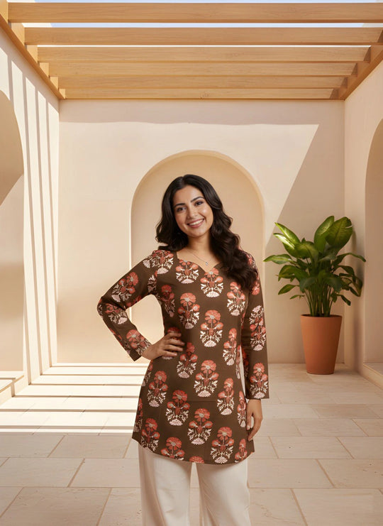 Woman wearing a patterned top in a well-lit room with a plant in the background