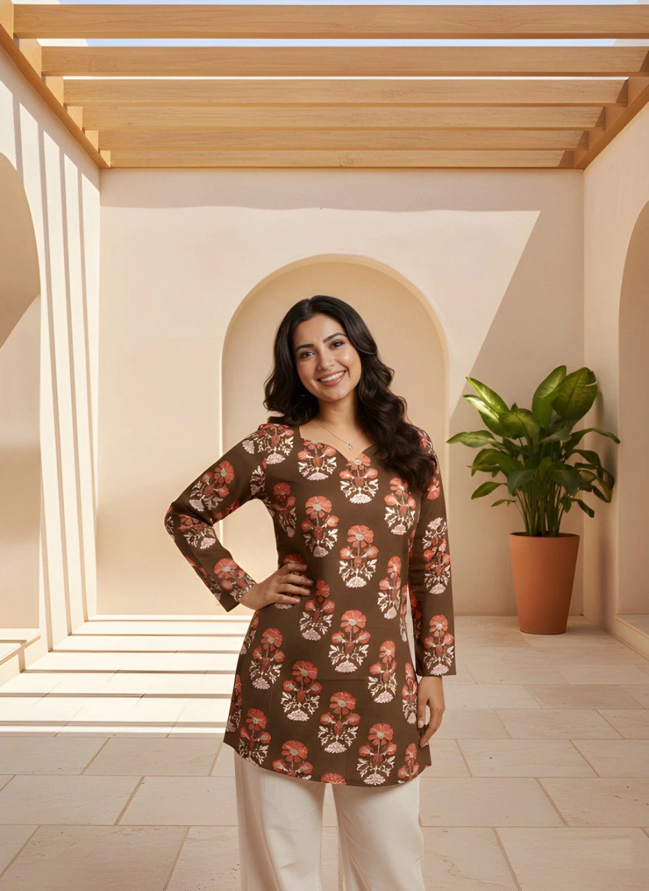 Woman wearing a patterned top in a well-lit room with a plant in the background