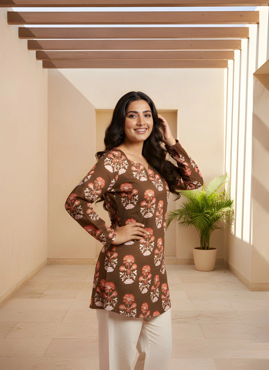 Woman wearing a floral patterned top in a well-lit room with wooden beams and a plant.