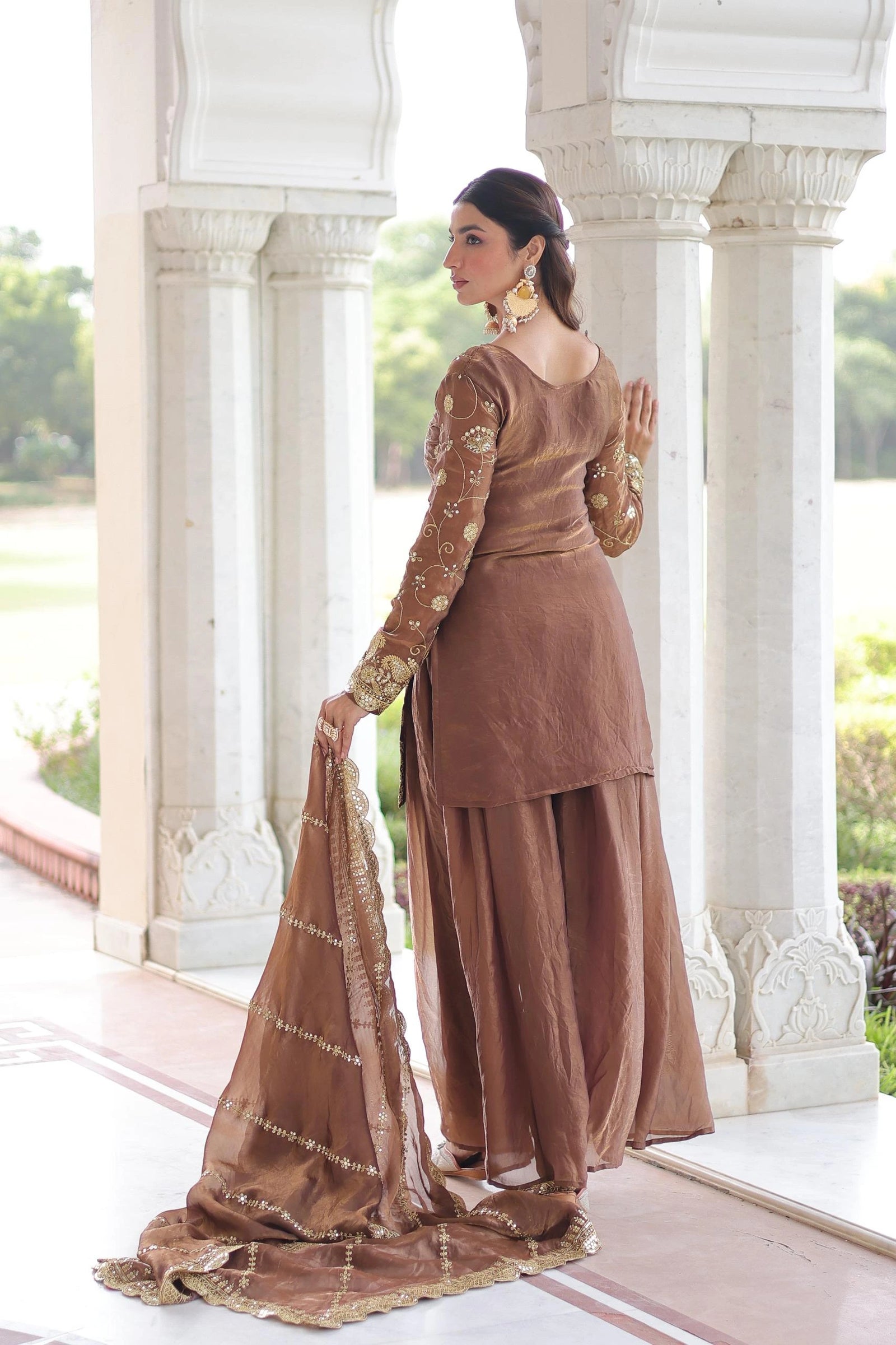 Woman in a brown traditional outfit standing in front of an architectural structure.