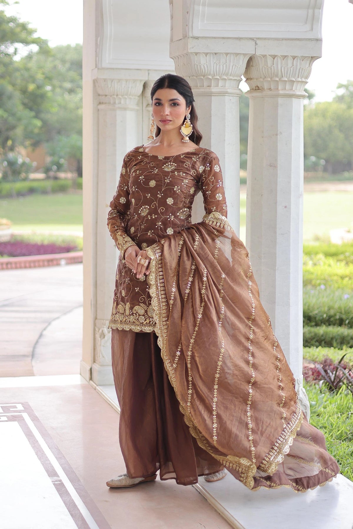 Woman in a traditional brown and gold outfit standing outdoors.