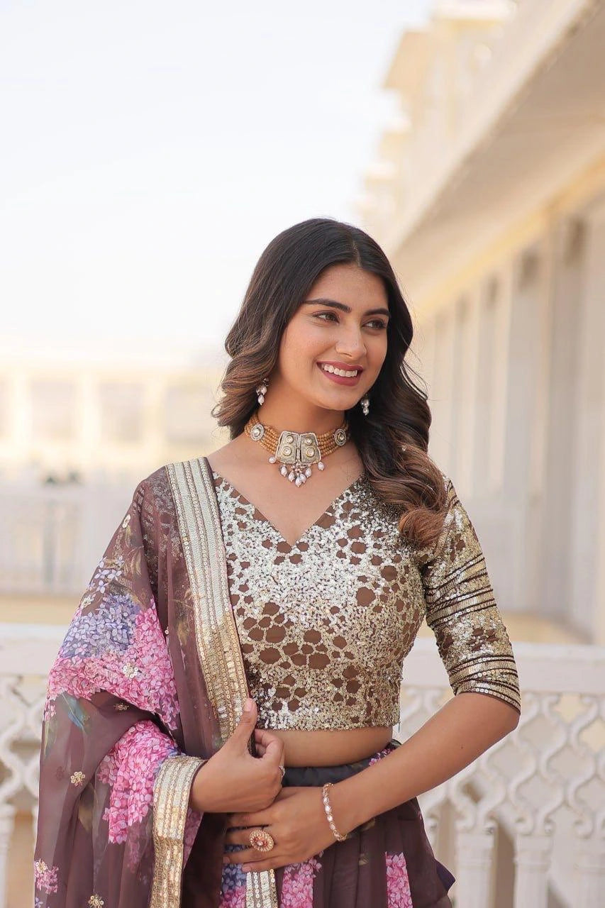 Woman wearing a traditional outfit with a decorative blouse and saree, standing in front of an architectural background.
