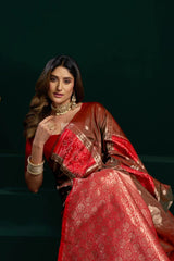 Woman wearing a red saree with gold patterns against a dark background