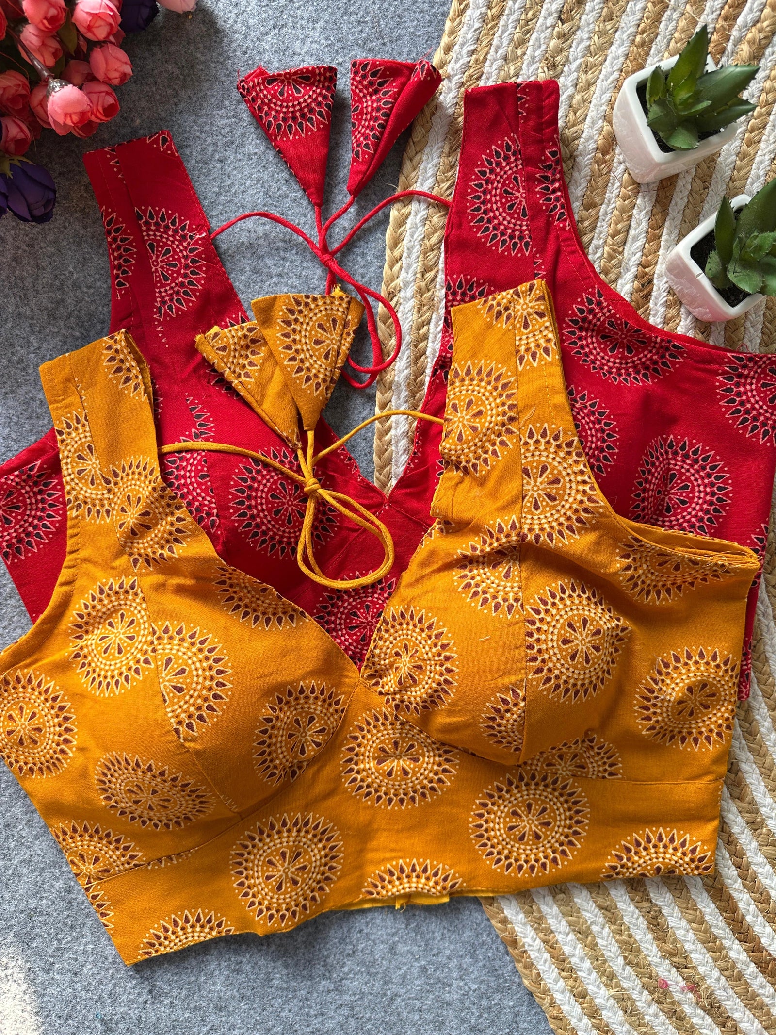 Red and yellow embroidered tops on a textured surface with flowers and plants in the background.