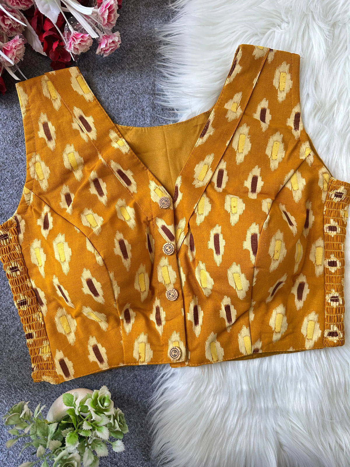 Yellow patterned top on a textured surface with flowers and greenery.