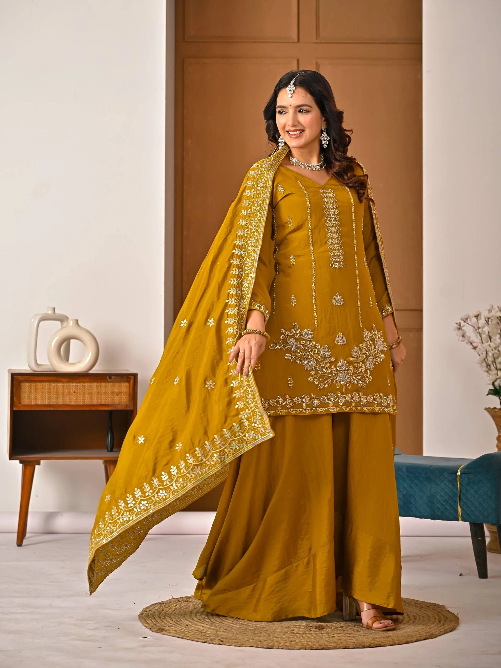 Woman in a mustard yellow traditional outfit with embroidery indoors.