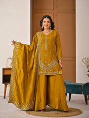 Woman in a mustard yellow traditional outfit with embroidery, standing indoors.