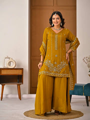 Woman in a mustard yellow traditional outfit with intricate patterns standing in a room.