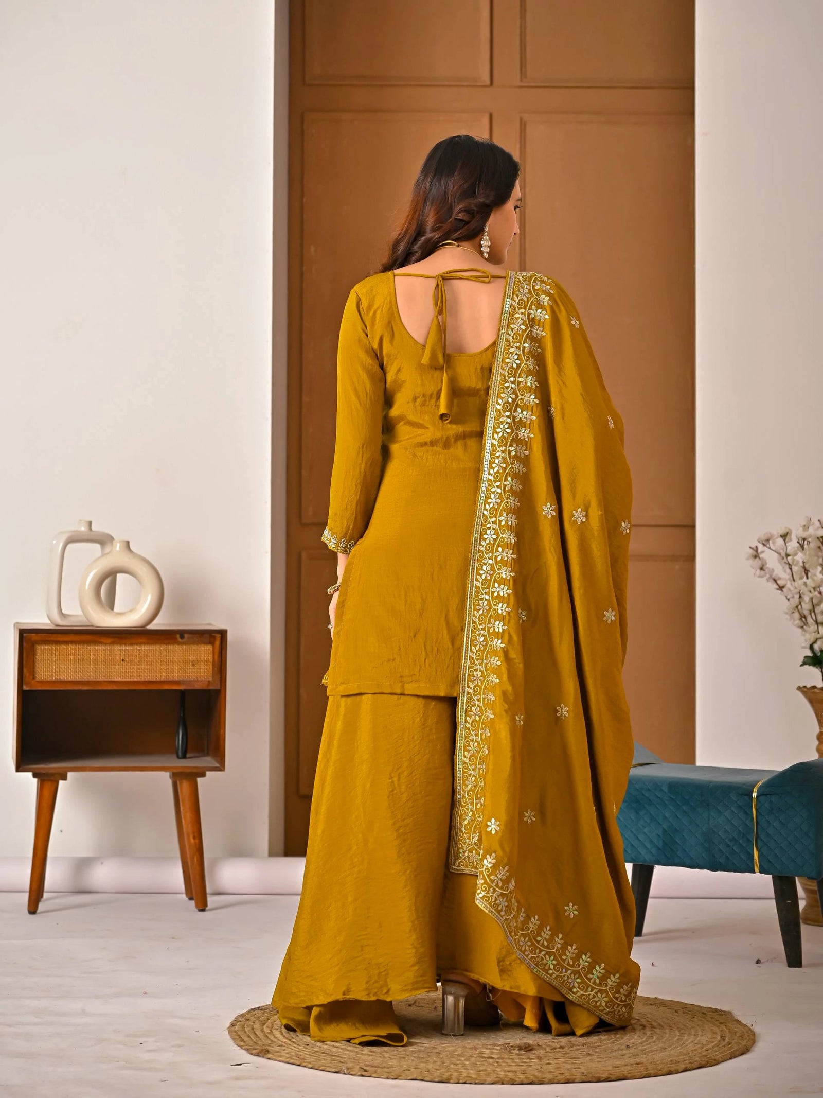 Woman in a yellow traditional outfit with a matching dupatta in a room setting.