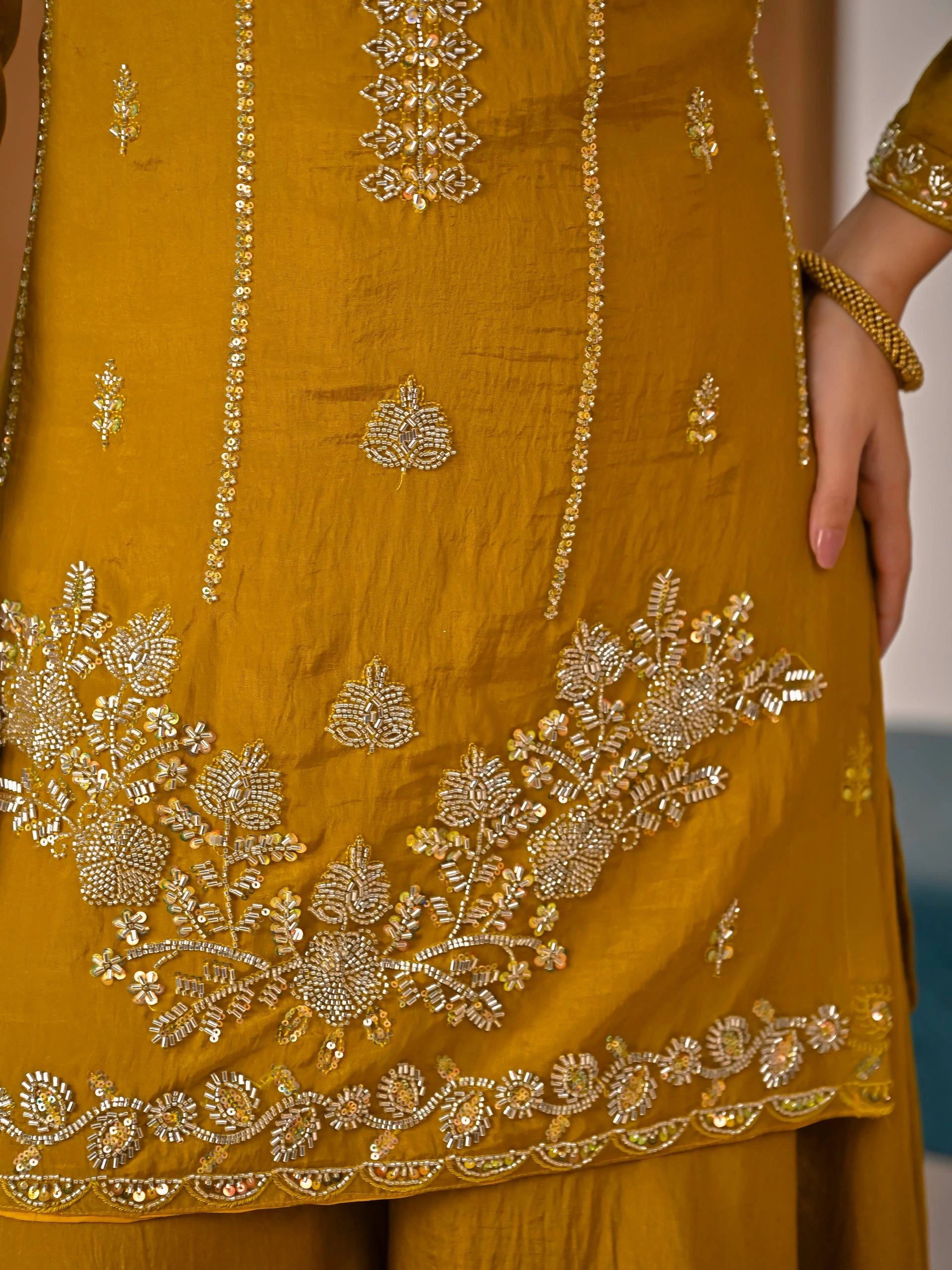 Close-up of a mustard yellow outfit with intricate gold embroidery.