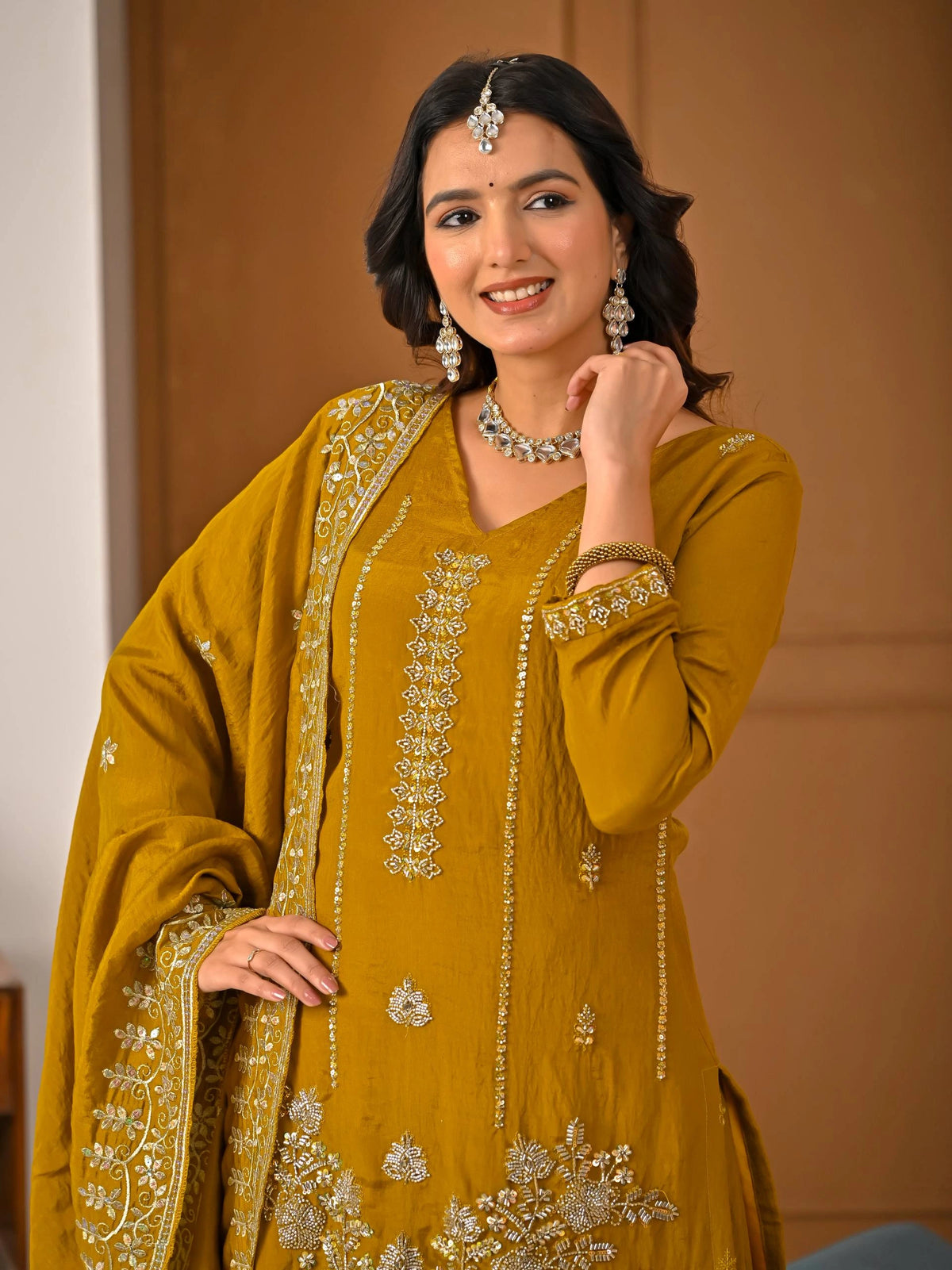 Woman wearing a mustard yellow traditional outfit with intricate embroidery, posing indoors.