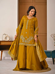 Woman in a mustard yellow traditional outfit with embroidery in a room setting.