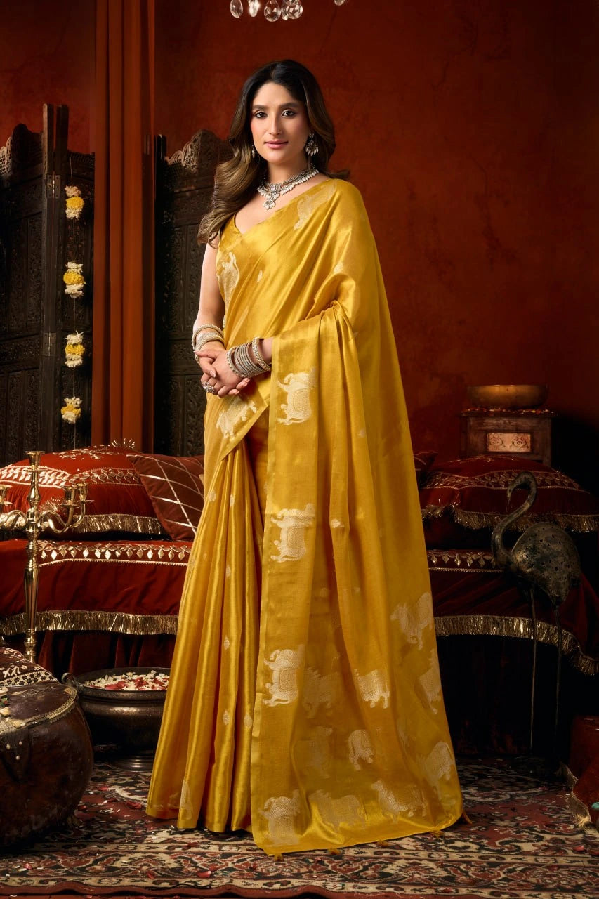 Woman in a yellow saree standing in an ornate room with decorative elements.