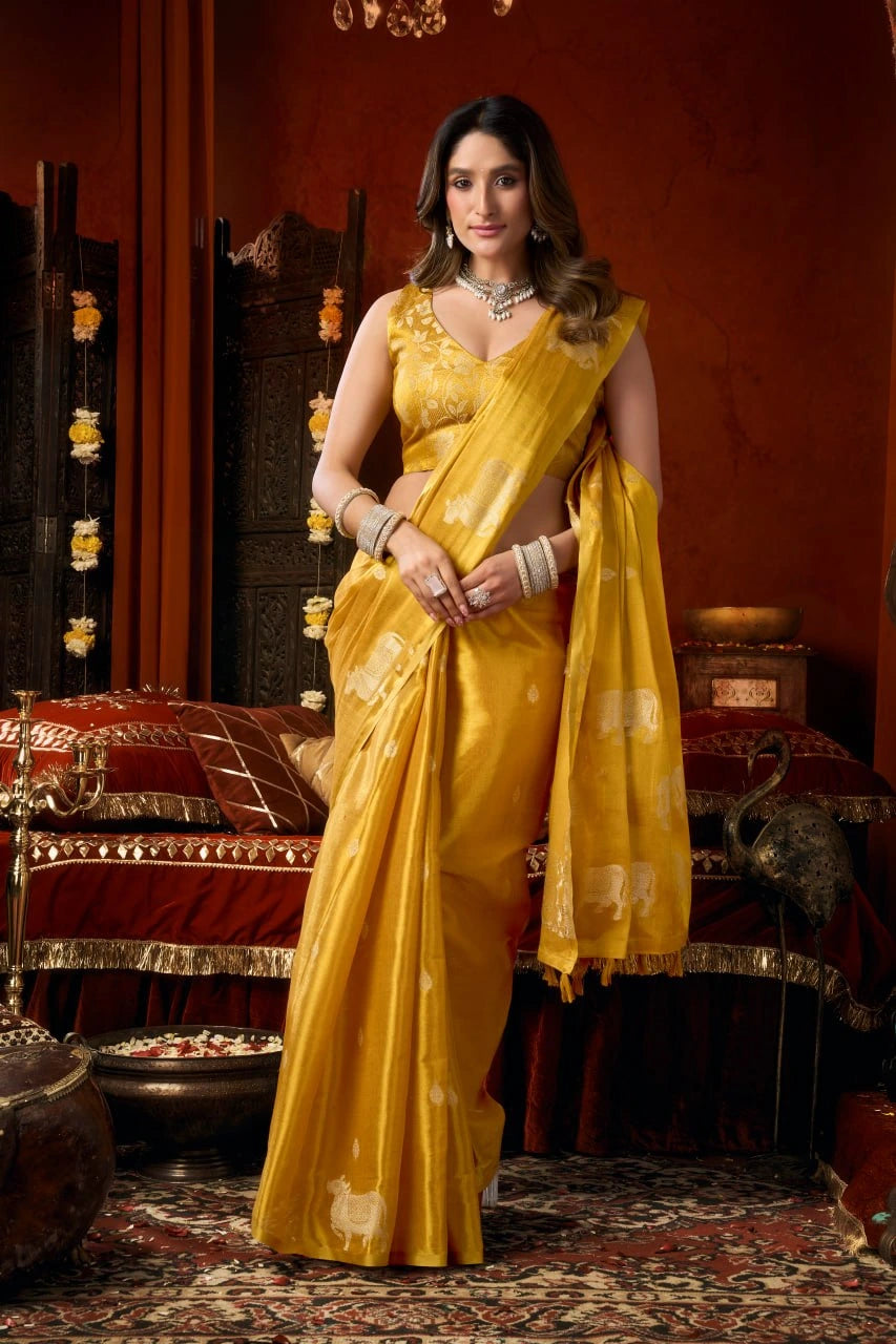 Woman in a yellow saree standing in an ornate room with red walls and patterned rug.