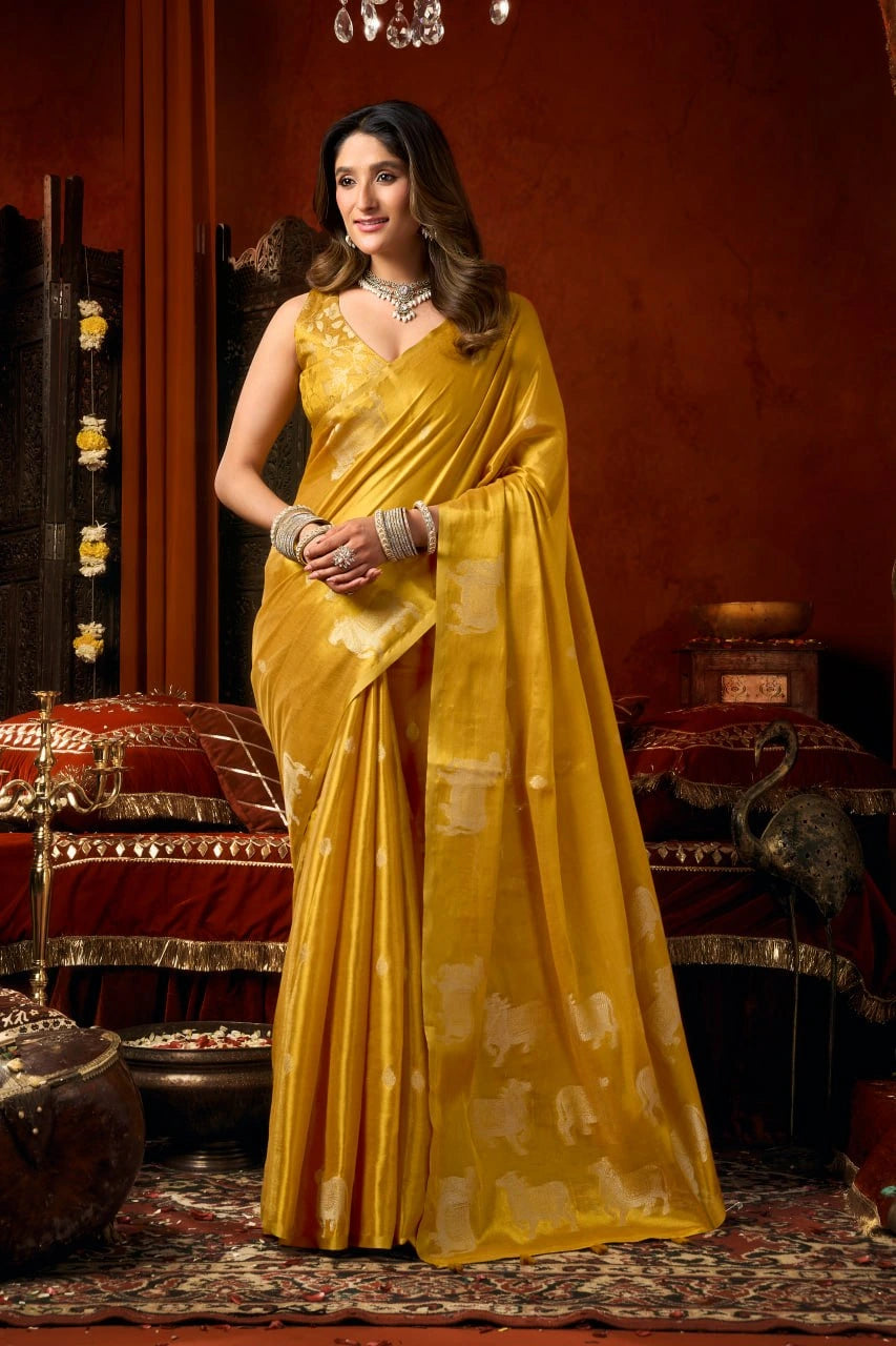 Woman in a yellow saree standing in an ornate room with red walls and decorative elements.