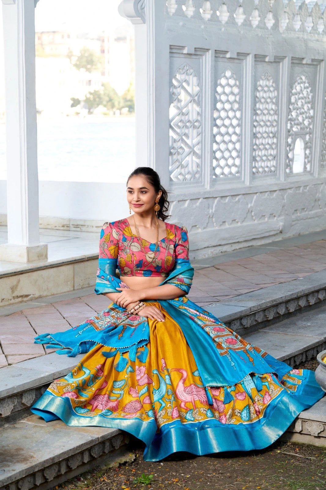 Elegant ethnic ensemble showcasing a printed mustard lehenga, multicolor floral blouse, and a contrasting blue dupatta with a lustrous zari border.